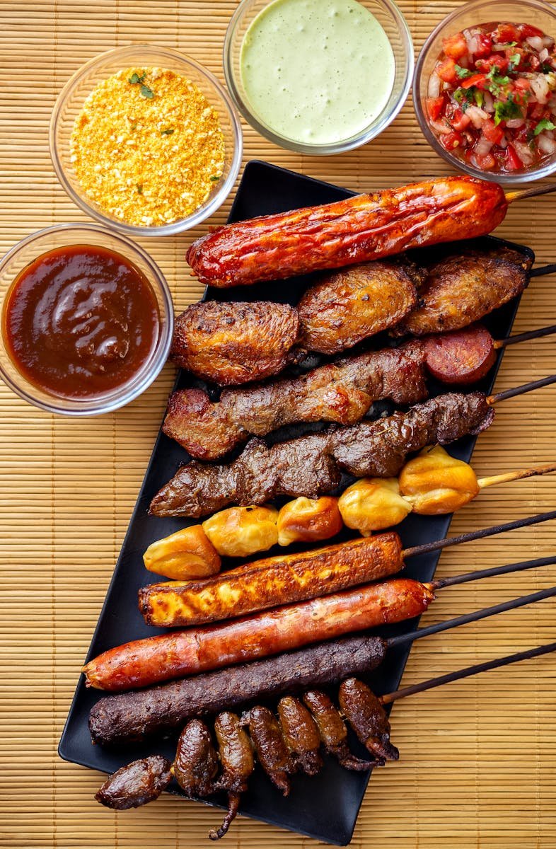 A mouthwatering platter of grilled skewers and dipping sauces on a bamboo mat.
