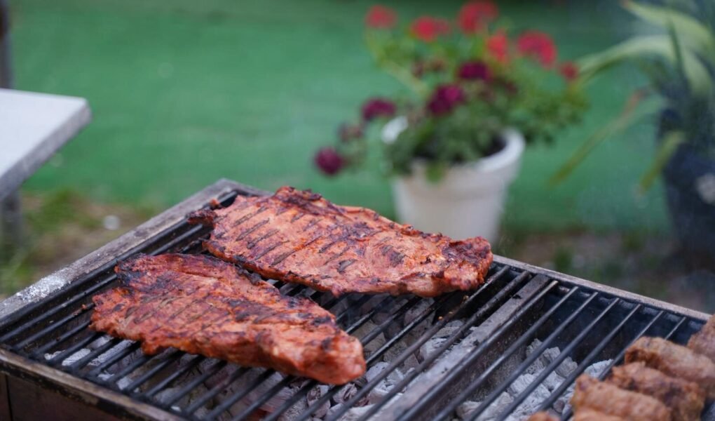 Juicy ribs sizzling on a charcoal grill in a garden setting. Perfect for summer BBQs.