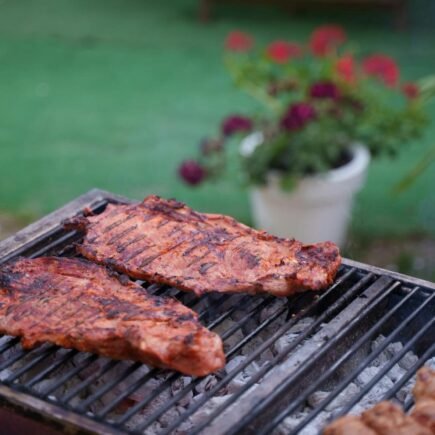 CHURRASCO: 3 RECEITA DE MOLHO DE ALHO PARA O SEU CHURRASCO Juicy ribs sizzling on a charcoal grill in a garden setting. Perfect for summer BBQs.
