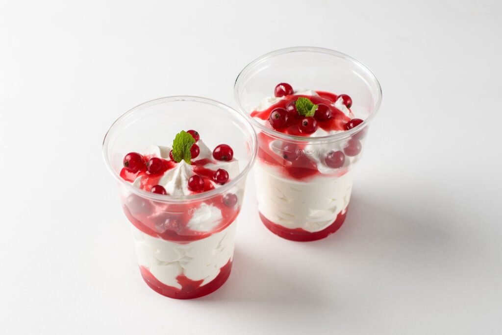 Two delicious red berry parfaits with cream, mint garnish in clear cups.