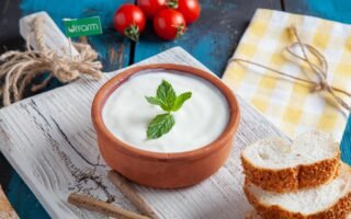 Authentic Turkish yogurt served in a clay bowl with mint, tomatoes, and sesame bread on rustic wooden board.
