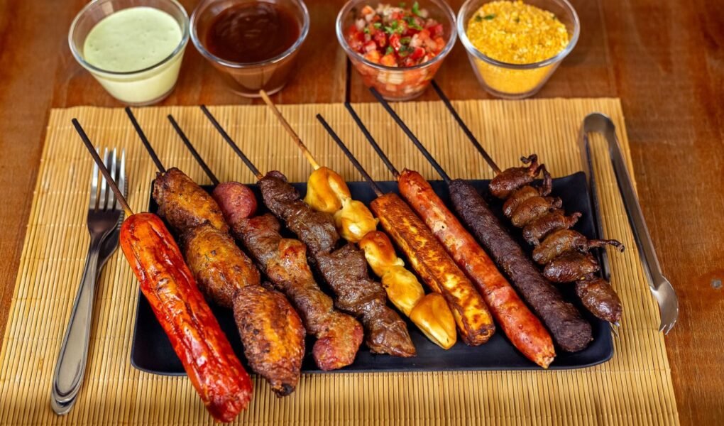 A variety of barbecued skewers with dips on a wooden table, perfect for outdoor dining.