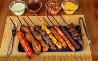 A variety of barbecued skewers with dips on a wooden table, perfect for outdoor dining.
