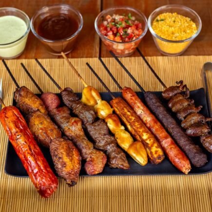 A variety of barbecued skewers with dips on a wooden table, perfect for outdoor dining.