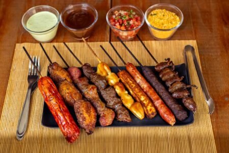 A variety of barbecued skewers with dips on a wooden table, perfect for outdoor dining.