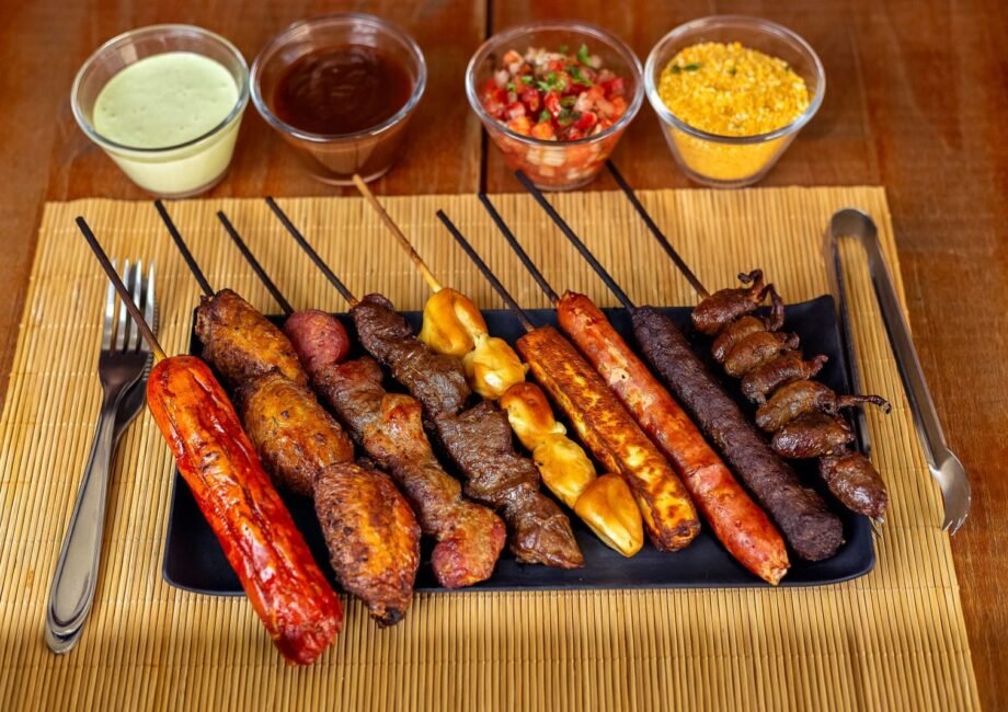 A variety of barbecued skewers with dips on a wooden table, perfect for outdoor dining.